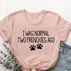 May include: A pink t-shirt with the text "I was normal two frenchies ago" and two black paw prints.