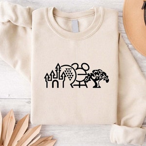 K&ouml;nnte beinhalten: Ein beiger Pullover mit einer schwarzen Grafik der ikonischen Disney World-Sehensw&uuml;rdigkeiten, darunter das Schloss von Aschenputtel, Spaceship Earth, der Mickey Mouse-Kopf und der Baum des Lebens.