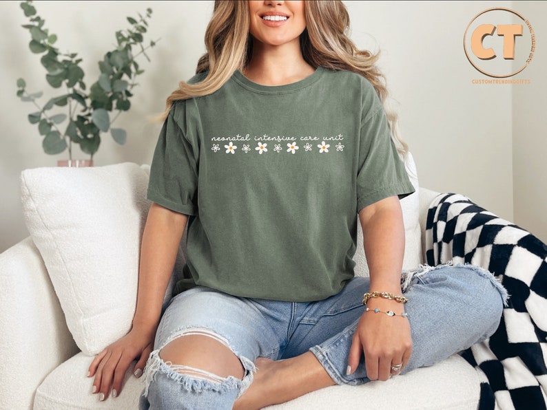 K&ouml;nnte beinhalten: Ein gr&uuml;nes T-Shirt mit dem Text "neonatal intensive care unit" und kleinen wei&szlig;en Blumen, die auf der Vorderseite aufgedruckt sind.
