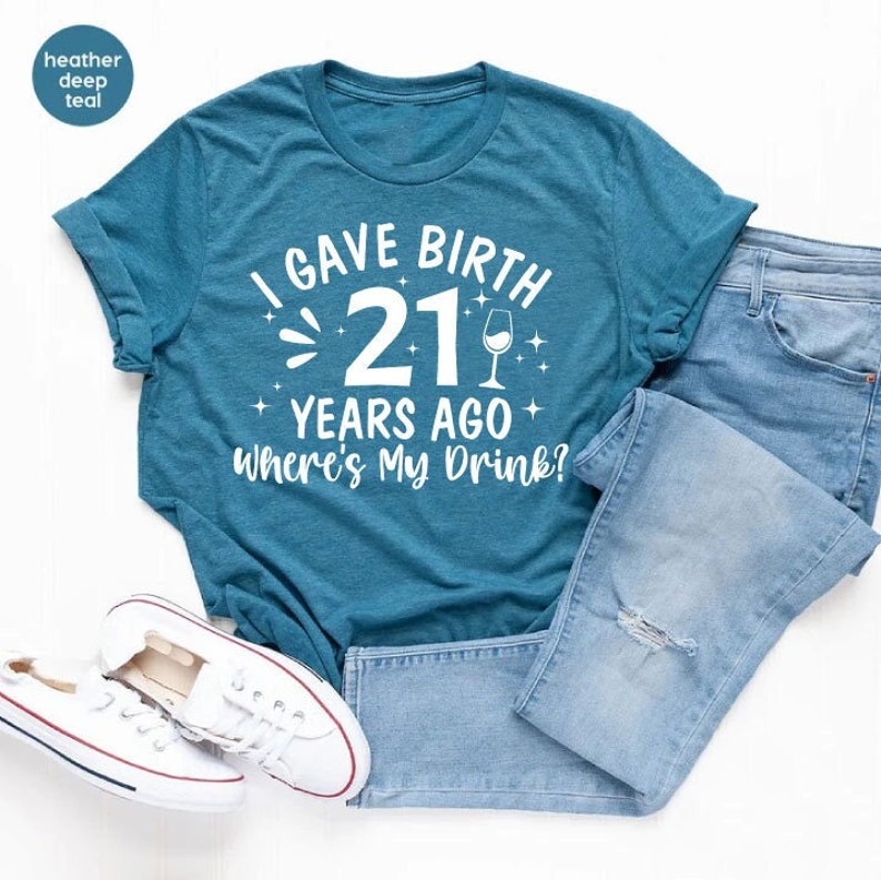 May include: A teal blue t-shirt with white text that reads "I gave birth 21 years ago where's my drink?" with a wine glass icon.