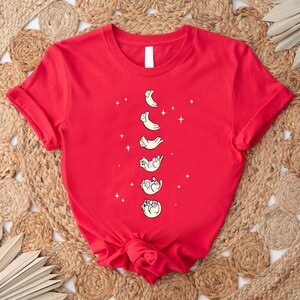 a red t - shirt with cats and the moon on it