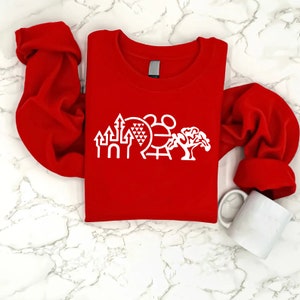 K&ouml;nnte beinhalten: Roter Langarm-Pullover mit einem wei&szlig;en Aufdruck des Disney World-Horizonts, einschlie&szlig;lich Cinderella's Castle, Spaceship Earth, Haunted Mansion und dem ikonischen Mickey Mouse-Kopf.