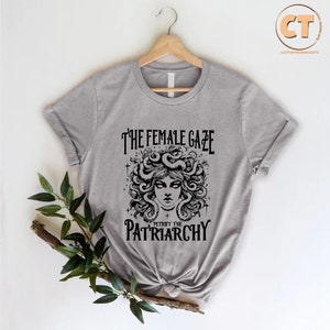 K&ouml;nnte beinhalten: Graues T-Shirt mit einer schwarzen Grafik einer Frau mit Schlangen als Haaren. Der Text lautet "The Female Gaze Petrify the Patriarchy."