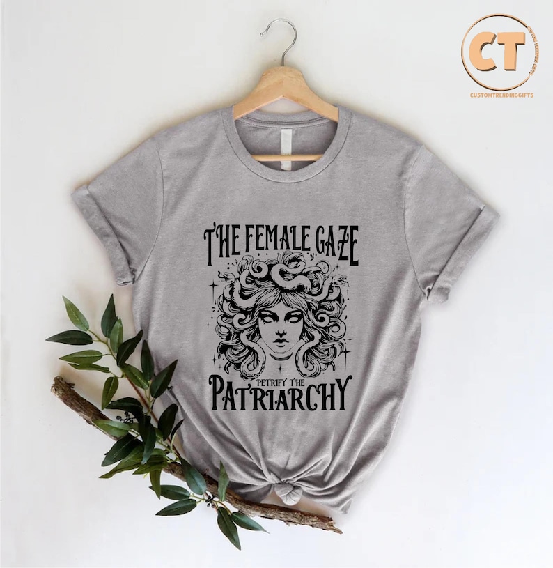 K&ouml;nnte beinhalten: Graues T-Shirt mit einer schwarzen Grafik einer Frau mit Schlangen als Haaren. Der Text lautet "The Female Gaze Petrify the Patriarchy."