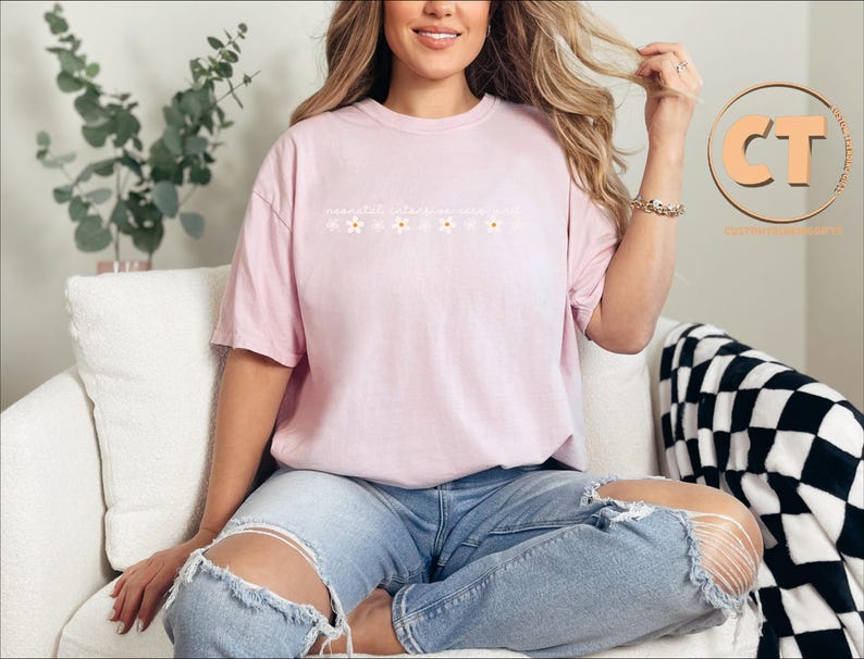 K&ouml;nnte beinhalten: Ein pinkfarbenes T-Shirt mit einem Blumendesign und dem Text "remarkable ordinary you". Das Model tr&auml;gt das Shirt mit einer blauen Jeans.
