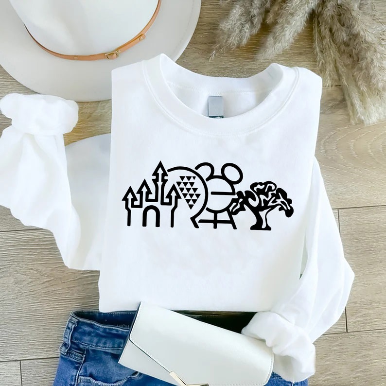 K&ouml;nnte beinhalten: Wei&szlig;es Sweatshirt mit einer schwarzen Grafik von ikonischen Disney World-Sehensw&uuml;rdigkeiten, darunter das Schloss von Aschenputtel, Spaceship Earth, das Mickey Mouse-Symbol und der Baum des Lebens.