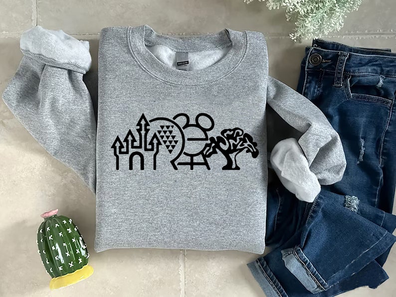K&ouml;nnte beinhalten: Ein graues Sweatshirt mit einer schwarzen Grafik der ikonischen Disney World-Sehensw&uuml;rdigkeiten, darunter das Schloss von Aschenputtel, Spaceship Earth, Mickey Mouse und ein Baum.