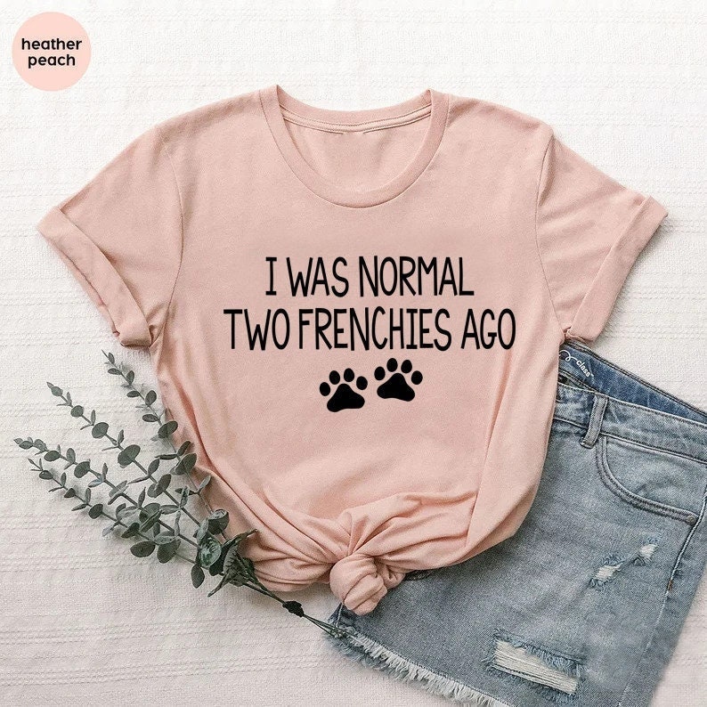 May include: A pink t-shirt with the text "I was normal two frenchies ago" and two black paw prints.