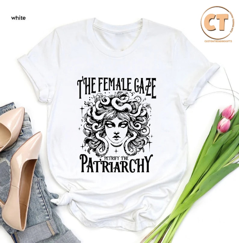 K&ouml;nnte beinhalten: Wei&szlig;es T-Shirt mit einer schwarz-wei&szlig;en Grafik einer Frau mit Schlangen als Haaren. Der Text "The Female Gaze" und "Petrify the Patriarchy" ist auf dem Shirt aufgedruckt.