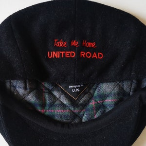 May include: Black wool newsboy cap with a red embroidered logo that says "Take Me Home UNITED ROAD" and a black and green plaid lining. The cap is designed in the U.K.
