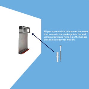 May include: A silver metal wall hanger with a rectangular top slot and a red bottom edge, accompanied by a wall screw and a plastic dowel. Text reads: All you have to do is to hammer the screw that comes in the package into the wall using a dowel and hang it on the hanger that comes ready for wall art.