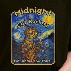 Può includere: T-shirt nero con un design stravagante di un gatto in una scena notturna stellata, con la scritta "Midnight Cat Society" e "Est. Under the stars". Il gatto è raffigurato in stile Van Gogh.