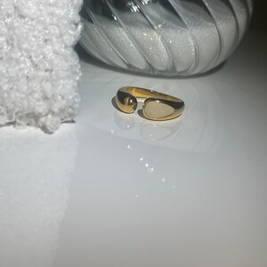 Peut inclure: Une bague en or avec une pierre ovale blanche. La bague est ouverte d'un c&ocirc;t&eacute; et a une boule ronde en or de l'autre c&ocirc;t&eacute;.