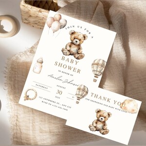 May include: A white baby shower invitation with a brown teddy bear, hot air balloons, and the text "Join us for a Baby Shower in honor of Amelia Johnson, Saturday, August 30, 2015, 123 Anywhere St., Any City, RSVP to 123-456-7895". A separate white thank you card features a brown teddy bear and the text "Thank You for showering our baby with love."