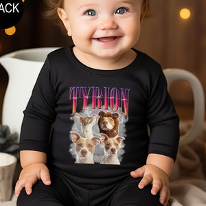 a baby sitting on a bed wearing a black t - shirt with a picture of