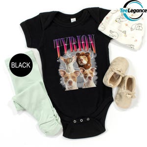 May include: Black baby onesie with a graphic of four dogs and the word "TYRION" in a colorful, retro font. The onesie is paired with a pair of light green leggings and a white beanie with a floral pattern.