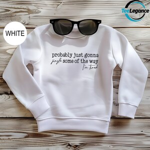 A white sweatshirt with the text "probably just gonna jingle some of the way I'm tired" printed on it, along with a pair of sunglasses placed on top of the sweatshirt.
