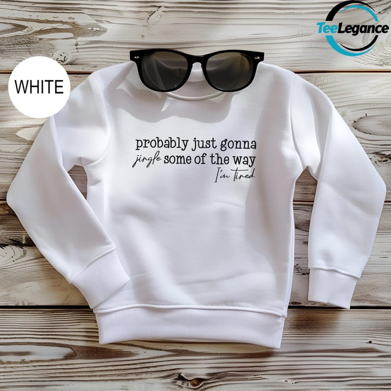 A white sweatshirt with the text "probably just gonna jingle some of the way I'm tired" printed on it, along with a pair of sunglasses placed on top of the sweatshirt.