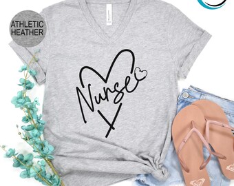 May include: Athletic heather gray V-neck t-shirt with a black heart design and the word "Nurse" in a handwritten font. The design includes a small heart and an "X" below the word. The shirt is paired with denim shorts and pink flip-flops.
