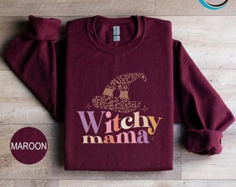 May include: Maroon sweatshirt with a witch hat graphic and the text "Witchy mama". The witch hat has a leopard print design. The sweatshirt is a crew neck style.