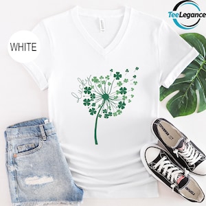 May include: White V-neck t-shirt with a green shamrock dandelion design and the word "lucky" written on the shirt.
