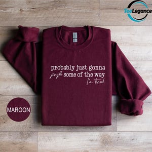 A maroon sweatshirt with the text "probably just gonna sing some of the way Tim I'm tired" printed on it, along with a small maroon circle with the text "MAROON" below it.