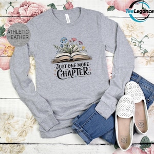 May include: A gray long-sleeve shirt with the text "Just One More Chapter" and a graphic of an open book with flowers on top.