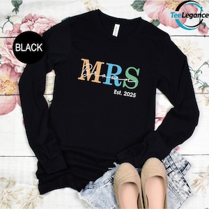 May include: Black long-sleeve shirt with the text "MRS" in colorful letters and "Est. 2025" below.