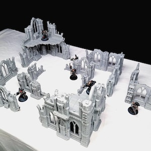 以下が含まれることがあります： グレーのゴシック様式のテーブルトップゲーム用地形セット。複数の建物の廃墟が含まれています。ミニチュアフィギュアが構造物内に配置され、戦闘シーンを暗示しています。セットには、アーチ、壁、その他の建築要素が含まれています。