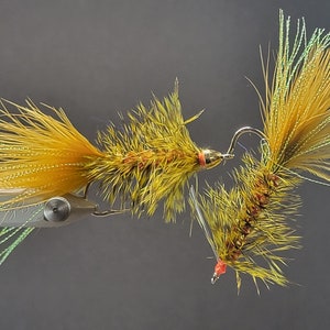 May include: Two yellow and green fly fishing lures with orange accents. The lures are tied with feathers and are attached to hooks.