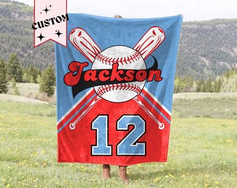 May include: A blue and red personalized baseball blanket with a baseball, bats, and the name "Jackson" and number "12" printed on it.
