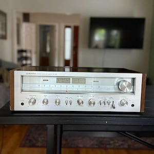May include: A Pioneer stereo receiver model SX-950 with a silver metal front panel, wooden side panels, two analog signal meters, a horizontal radio tuning dial, and multiple circular control knobs and toggle switches for audio adjustment.