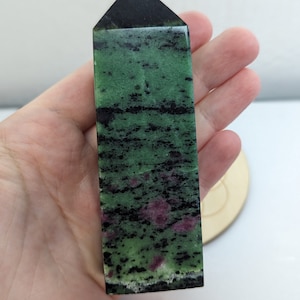 May include: A green, black and pink zultanite crystal point. The crystal is polished and has a pointed tip. It is approximately 5 cm tall.