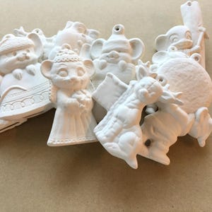 Peut inclure: Une collection d'ornements en céramique blanche non peinte représentant divers personnages animaux, dont des souris et un renne, chacun doté d'un petit trou au sommet pour suspendre. Ces figurines en biscuit ont des textures moulées détaillées.