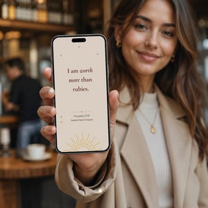 May include: A smartphone displaying a beige screen with the text I am worth more than rubies, Proverbs 31:10, and Grateful Heart Company, featuring a gold sunburst graphic at the bottom and small star accents on a clean, minimalist digital interface.