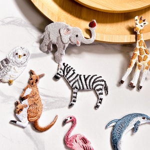 Peut inclure: Un ensemble de patchs brodés thermocollants représentant différents animaux, dont un zèbre, un éléphant, un kangourou, un hibou, un flamant rose, une girafe et un dauphin. Les patchs sont parfaits pour ajouter une touche de fantaisie aux vêtements, aux sacs ou à d'autres articles en tissu.