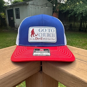 May include: A blue and white trucker hat with a red brim. A rectangular patch on the front features a red silhouette of a figure with a scythe and the text GO TO CHURCH Or the Devil Will Get You! A black Richardson 112 Original sticker is on the brim.