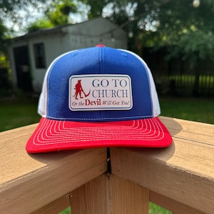 May include: A blue and white trucker hat with a red brim. The front features a rectangular patch with a red silhouette of a figure holding a pitchfork and the text: GO TO CHURCH Or the Devil Will Get You! in blue and red lettering.