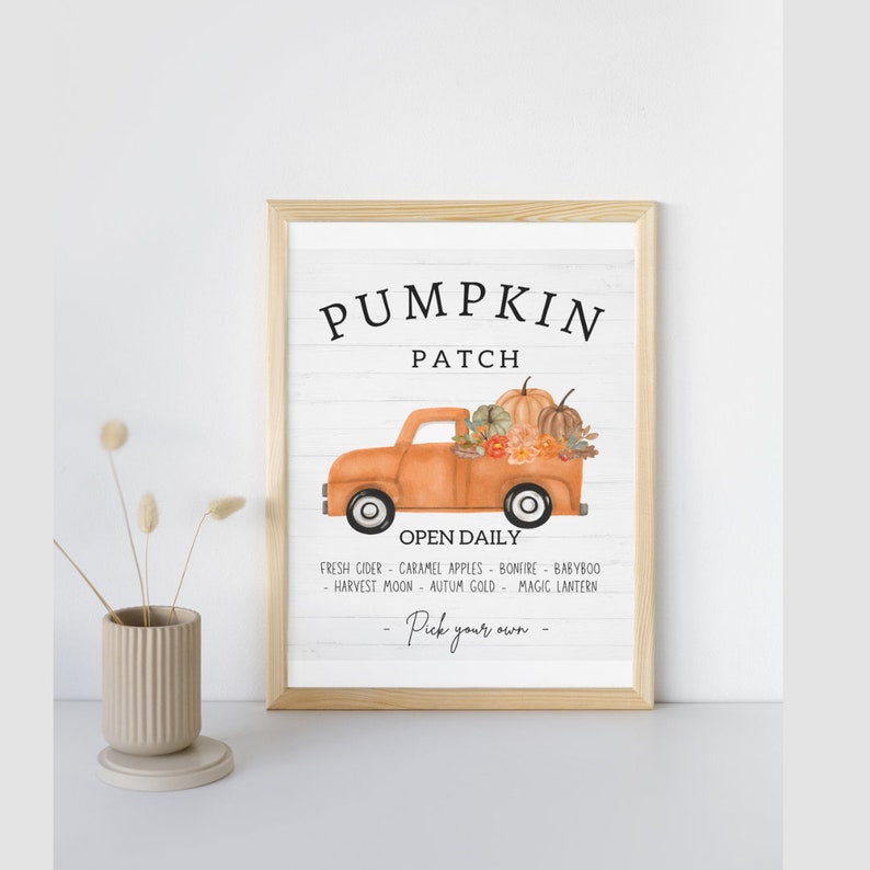 May include: A framed print with a light wood frame. The print features the words "Pumpkin Patch" above an orange truck filled with pumpkins and flowers. Below the truck, it reads "Open Daily" and a list of fall activities.