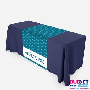 Pode incluir: Um corredor de mesa turquesa com a palavra "MODERE." impressa em branco sobre uma toalha de mesa azul marinho. O corredor de mesa é impresso com a palavra "MODERE" repetida em um padrão.