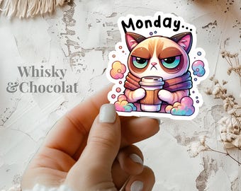 May include: A white sticker featuring a grumpy cat cartoon holding a cup of coffee. The cat is wearing a scarf and the sticker reads "Monday..." in pink lettering. The background is a colourful swirl of pink, blue and yellow.