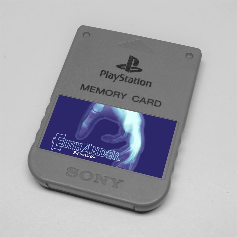 May include: A gray PlayStation memory card with the PlayStation logo and the text "MEMORY CARD". The card features a blue label with the game title "Einh&auml;nder" and a graphic of a hand. The SONY logo is at the bottom.