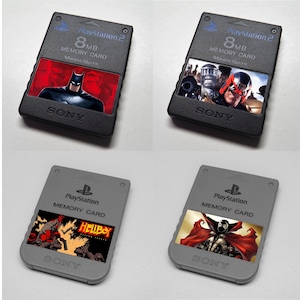 May include: Four PlayStation 2 memory cards. Two are black with superhero graphics and the text "PlayStation 2 8MB Memory Card Magic Gate". The other two are gray with comic book character graphics and the text "PlayStation Memory Card".