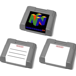 Puede incluir: Tres cartuchos de juego grises de Nintendo 64. Un cartucho tiene el logotipo y el texto de Nintendo 64. Los otros dos cartuchos tienen una etiqueta blanca con el logotipo de Nintendo. Una etiqueta tiene tres líneas horizontales.