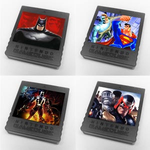 May include: Four Nintendo GameCube game cartridges featuring comic book characters. The cartridges display Batman, Superman, and other heroes. The cartridges are gray with the words "NINTENDO GAMECUBE" embossed on the front.