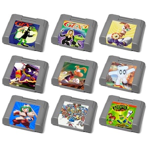 May include: Nine gray Nintendo 64 game cartridges are displayed, each with colorful game art. The cartridges feature various game titles and characters, including a lizard, a worm, and other animated figures. The games are arranged on a white surface.