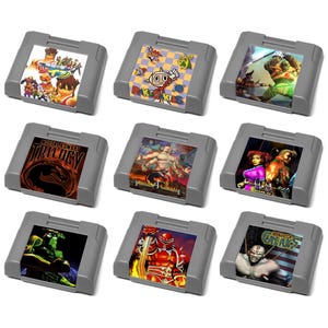 May include: Nine grey video game cartridges with colourful game art labels. The labels feature various characters and game titles. The cartridges are arranged in a grid pattern against a white background. The games appear to be from the 1990s.