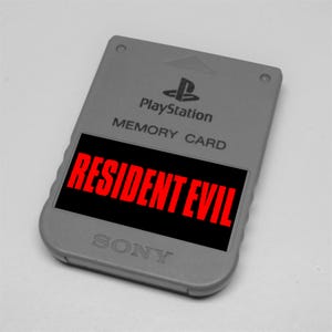 Puede incluir: Una tarjeta de memoria gris de PlayStation con el texto "RESIDENT EVIL" en rojo sobre un fondo negro. La tarjeta también presenta el logotipo de PlayStation, las palabras "MEMORY CARD" y el logotipo de SONY.