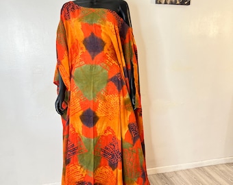 Könnte beinhalten: Ein orange, grün und lila gemustertes Kleid mit One-Shoulder-Design. Das Kleid wird auf einer schwarzen Schaufensterpuppe präsentiert. Das Kleid hat eine fließende, lockere Passform und ist bodenlang.