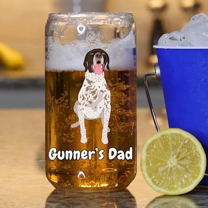 May include: A clear glass beer can with a brown and white dog illustration and the text "Gunner's Dad". The can is filled with a golden beer and has a white foam head.